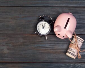 Tirelire cochon avec des billets et un réveil sur un fond en bois